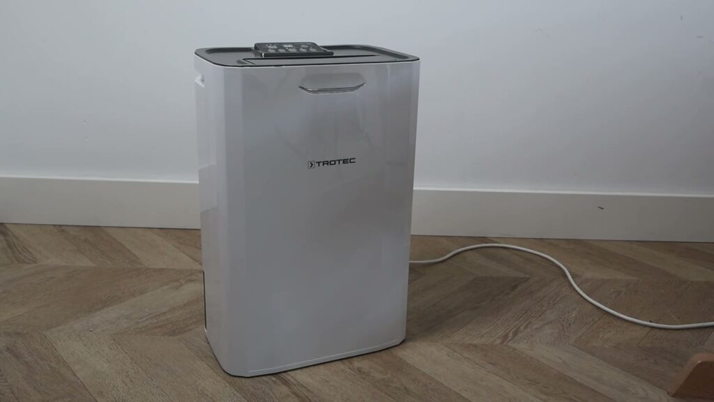 Déshumidificateur à adsorption Trotec TTR 57 E posé sur un parquet, contre un mur blanc